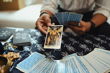 Close up view of hand holding a tarot card The Devil over table covered with a mystical cloth