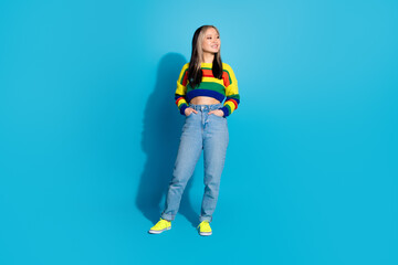 Full size photo of pretty young girl hands pockets look empty space wear trendy striped outfit isolated on blue color background