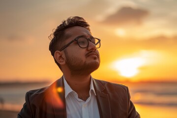 Fototapeta premium Portrait of a content indian man in his 20s sporting a stylish leather blazer isolated on vibrant beach sunset background
