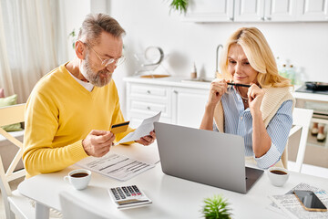 A mature couple in cozy homewear deeply engrossed in reviewing paperwork together at a table in...