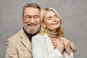 Elegant, mature, loving couple poses in debonair attire against a gray backdrop.