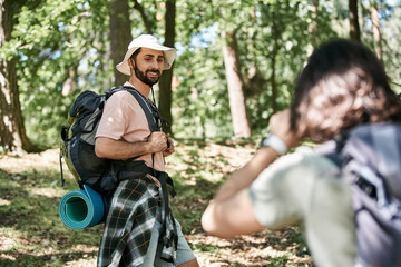 A young gay couple hikes through a lush forest on a sunny summer day.