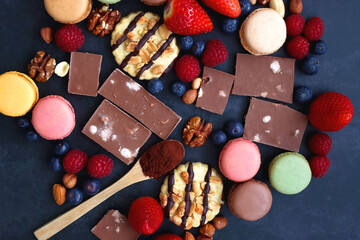Macarons, chocolate, cookies, berries and various nuts on dark blue background. Top view.