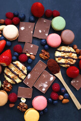 Macarons, chocolate, cookies, berries and various nuts on dark blue background. Top view.