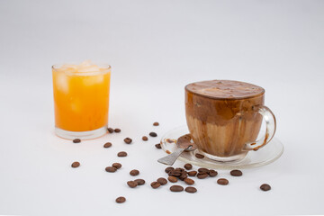 Home made dalgona coffee with scattered coffee beans and a glass of fresh orange juice ,on gray background