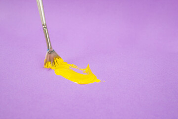 Yellow acrylic pain stroke with a paint brush on purple color background, soft focus close up
