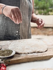 Woman baker with sprinkles flour on homemade pizza dough.
