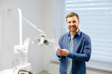Obraz premium Handsome male patient looking at his beautiful smile standing at the dental office