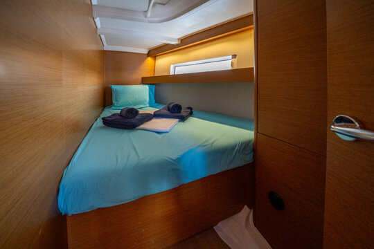 Sailing yacht interior. Double cabin on a charter yacht. Bareboat yacht interior - wood trim, light mattress and bedding, plenty of light from portholes. Comfortable berth for cruise on seas, oceans