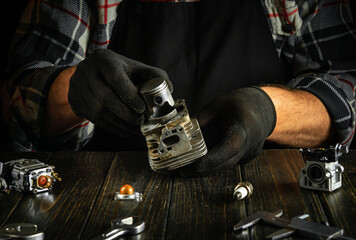 Repair of a chainsaw engine after a breakdown by the hands of a master on a table in a workshop.