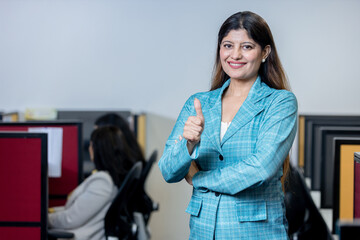 Obraz premium happy young indian woman gesturing thumbs up in office and looking at camera. business, success and corporate concept.