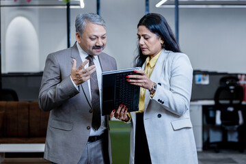 Young indian professional woman showing businessman company growth using digital tablet in corporate office. workplace and business concept.