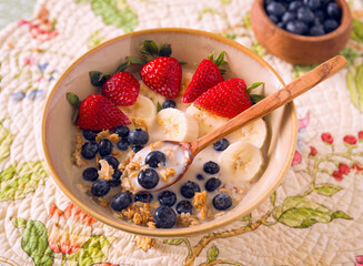 Plant based breakfast of organic granola, almond milk, strawberries, banana, and blueberries in a wooden bowl with a wooden spoon; copy space