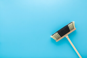 New white black broom with wooden stick on light blue table background. Pastel color. Closeup....