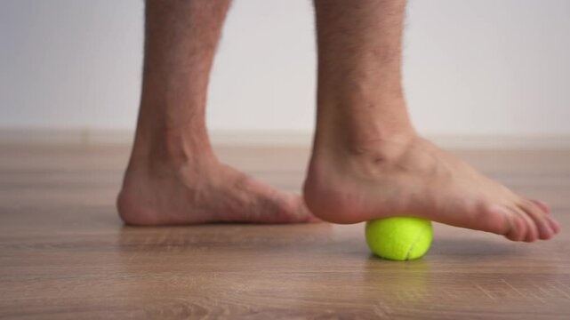Close-up of Male Legs Doing Special Exercises with a Tennis Ball to Treat Flat Feet. Concept of Therapeutic Physical Culture. Foot Health.