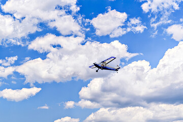 Single-engine ultralight airplane flying in the blue sky with white clouds	