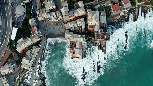 Top down aerial view of waves crashing into Genoa coastline lined with buildings