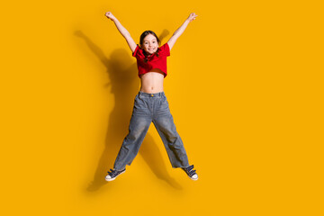 Full length portrait of cute little girl jump raise fists wear t-shirt isolated on yellow color background