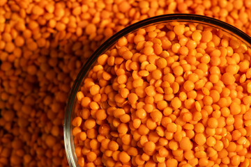 Raw red lentils are scattered out of the glass bowl