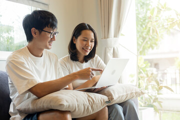 close up couple asian man and woman sitting together on couch and open laptop to consult each other about marriage and family planning for relationship and lifestyle concept