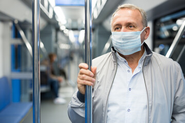 Mature passenger wearing protective mask rides in an underground metro car