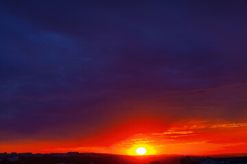 Beautiful sunset with a large orange sun in the sky. The sky is dark blue with some clouds. Awesome sunset over the city 
