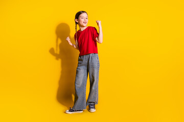 Full length portrait of cute little girl raise fists wear t-shirt isolated on yellow color background