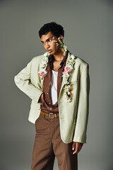 A young African American man in a stylish green blazer with flowers adorning his neck and face, posed against a grey background.