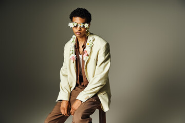 A young African American man poses in a stylish blazer adorned with flowers, radiating confidence and beauty.