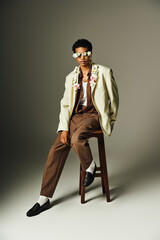 A young African American man poses in a stylish blazer, adorned with flowers, against a grey...