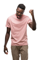 Naklejka premium Young african american man wearing pink t-shirt angry and mad raising fist frustrated and furious while shouting with anger. Rage and aggressive concept.