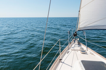 Obraz premium White yacht sailing on a sunny summer day. Top down view from the deck to the bow, mast and sails. Waves and water splashes. Clear blue sky. Gulf of Finland