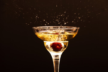 glass with splashes of champagne from cherry berries on a dark background.