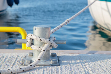 White rope with tied around a cleat on a pier. Nautical mooring rope