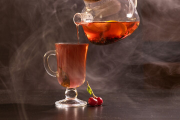 aromatic, fruity tea from oranges, lemons, currants, cherries is poured into a cup on a dark background.