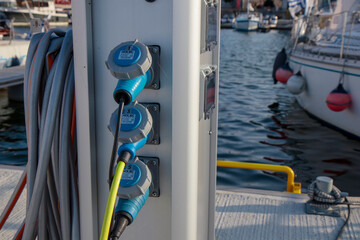 Charging and water station for boats, electrical outlets to charge ships in harbor, water vent and hose. Shore in marina jetty. Electrical power and drinking sweet water point on pier near sea coast