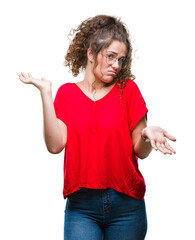 Beautiful brunette curly hair young girl wearing glasses over isolated background clueless and...