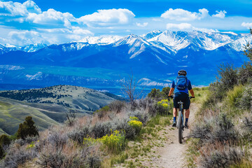 Fototapeta premium A man mountain biking on a rugged trail, with snow-capped peaks in the distance.
