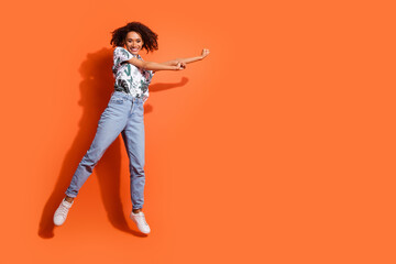 Full body length photo of american woman in jeans and summer stylish shirt jumping air discotheque party isolated on orange color background