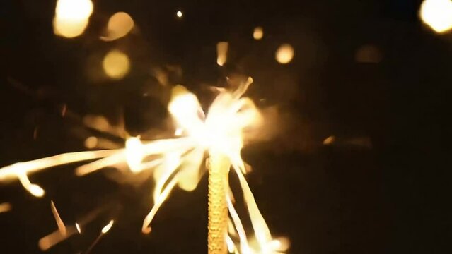 Slow motion close up of a sparkler that lights up function sparks against a black background.