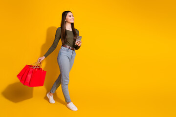 Full length photo of lovely teen lady go shopper device look empty space dressed stylish khaki garment isolated on yellow color background
