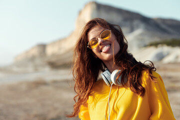 Woman in yellow shirt and sunglasses standing on beach overlooking distant mountain on sunny day