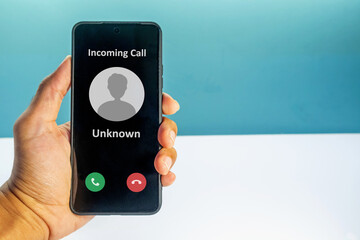 Hand holding a smartphone with incoming call from unknown number on the screen. Spammer incoming...