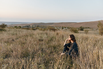 Serene woman sitting in lush field with majestic mountains in the distance under clear blue sky