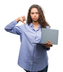 Young hispanic woman holding computer laptop with angry face, negative sign showing dislike with...