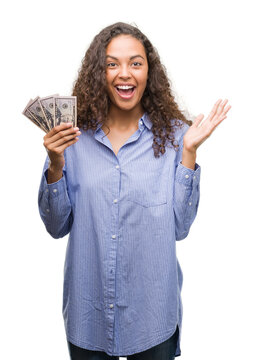Young hispanic woman holding dollars very happy and excited, winner expression celebrating victory screaming with big smile and raised hands