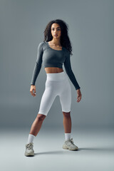 A young African American woman wearing white athletic shorts stands on a grey background.
