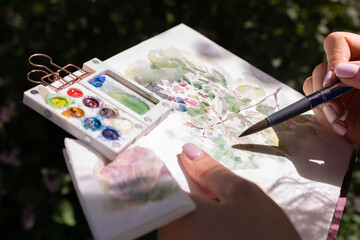 Watercolor painting in women hands. Female artist drawing in the dark of botanical garden and park,...