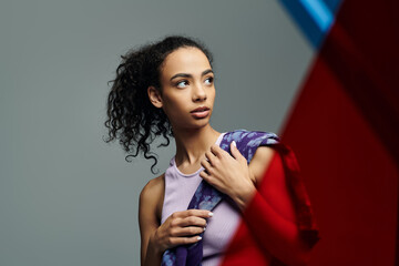 Naklejka premium A young woman with curly hair and a determined look holds a colorful scarf, showing off her athletic build.