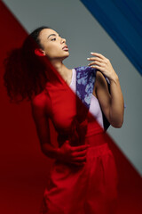 A young woman, posing with colorful glass panels behind her in a studio.